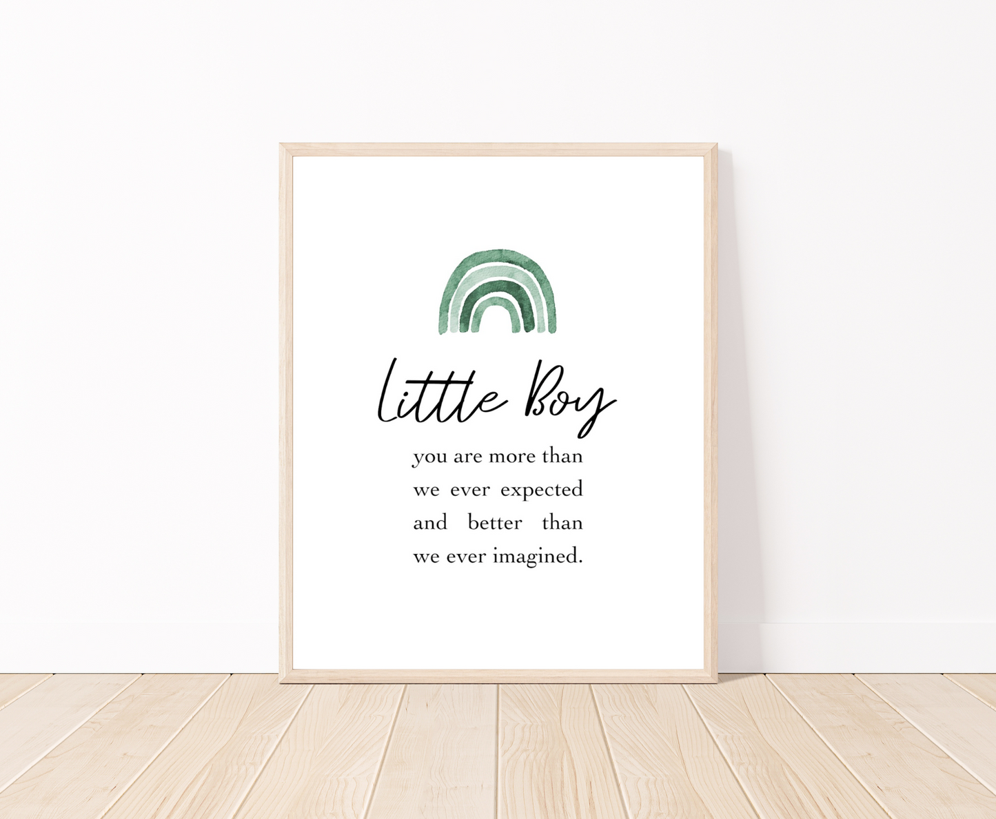 A frame showing a graphic for a little boy’s room displaying a rainbow design in different shades of green and includes a piece of writing that says: Little boy, you are more than we ever expected and better than we ever imagined. The frame is placed on a parquet floor.