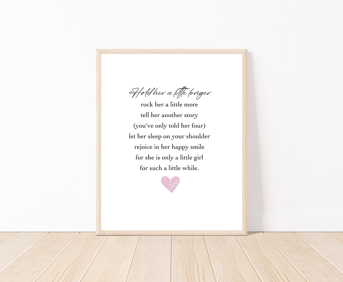 A digital print placed on a white wall and parquet flooring that has a pink heart at the bottom, and a piece of writing that says: Hold her a little longer, rock her a little more, tell her another story, (you have only told her four), let her sleep on your shoulder, rejoice in her happy smile, for she is only a little girl, for such a little while.