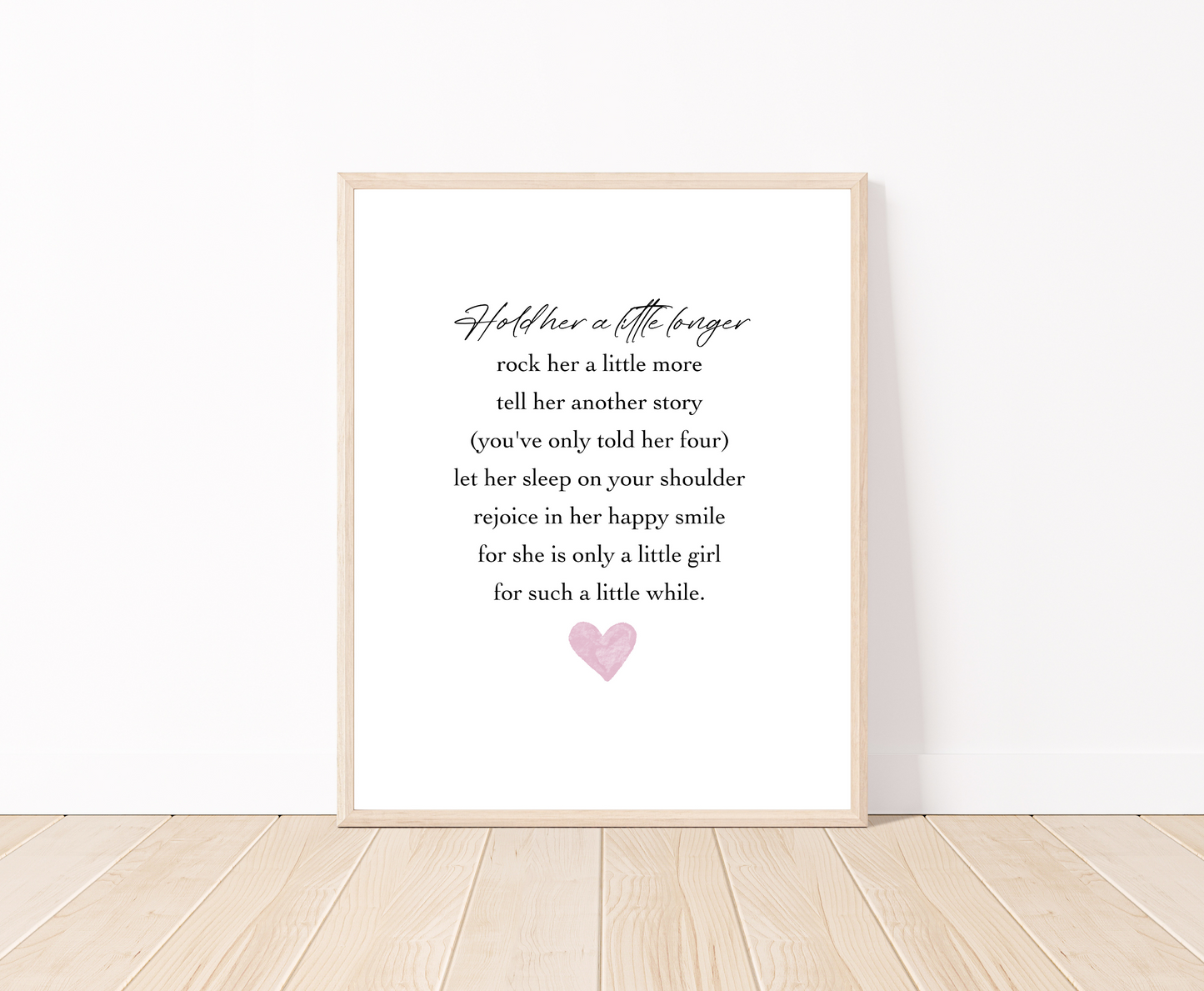 A digital print placed on a white wall and parquet flooring that has a pink heart at the bottom, and a piece of writing that says: Hold her a little longer, rock her a little more, tell her another story, (you have only told her four), let her sleep on your shoulder, rejoice in her happy smile, for she is only a little girl, for such a little while.