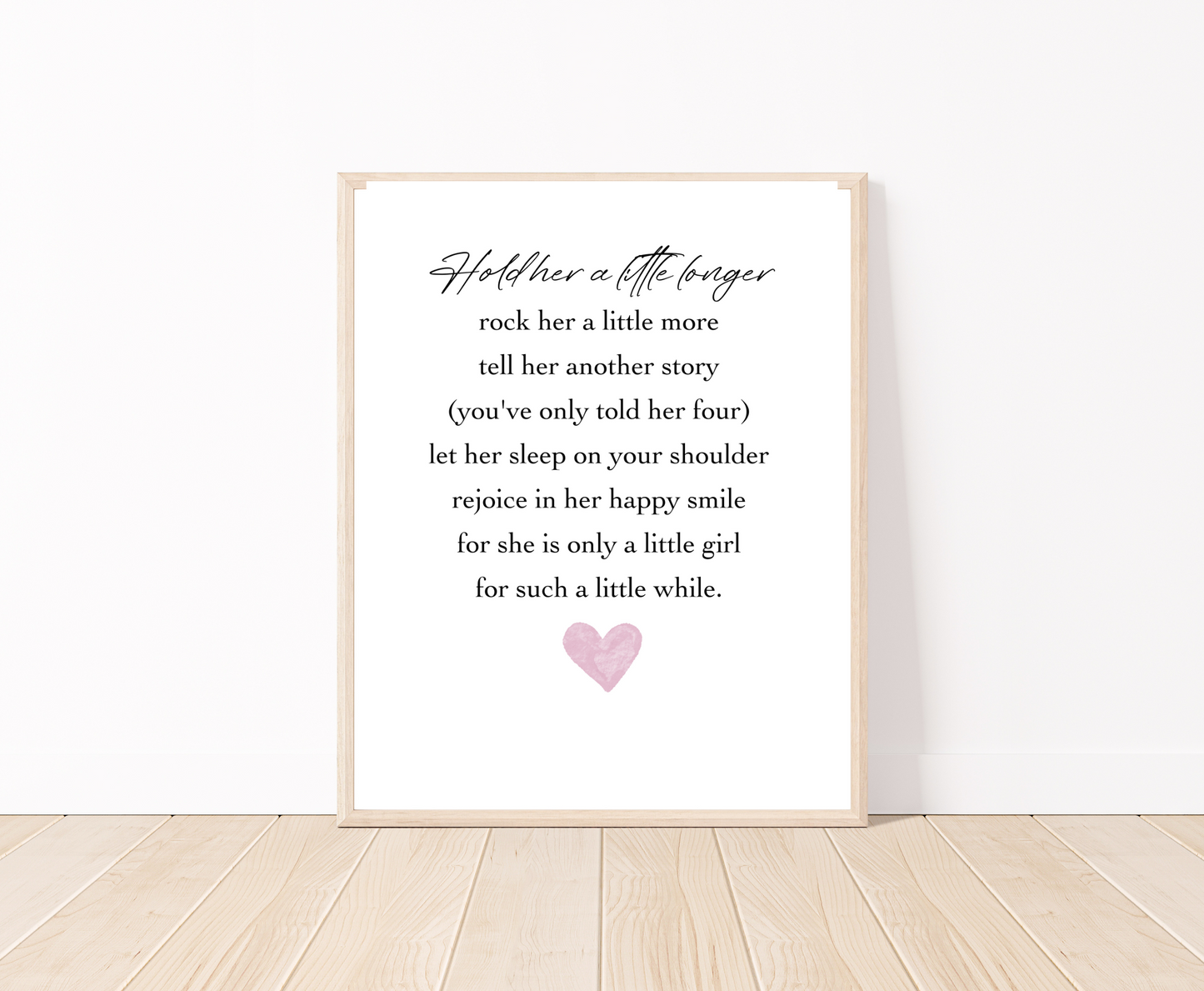 A digital print placed on a white wall and parquet flooring that has a pink heart at the bottom, and a piece of writing that says: Hold her a little longer, rock her a little more, tell her another story, (you have only told her four), let her sleep on your shoulder, rejoice in her happy smile, for she is only a little girl, for such a little while.