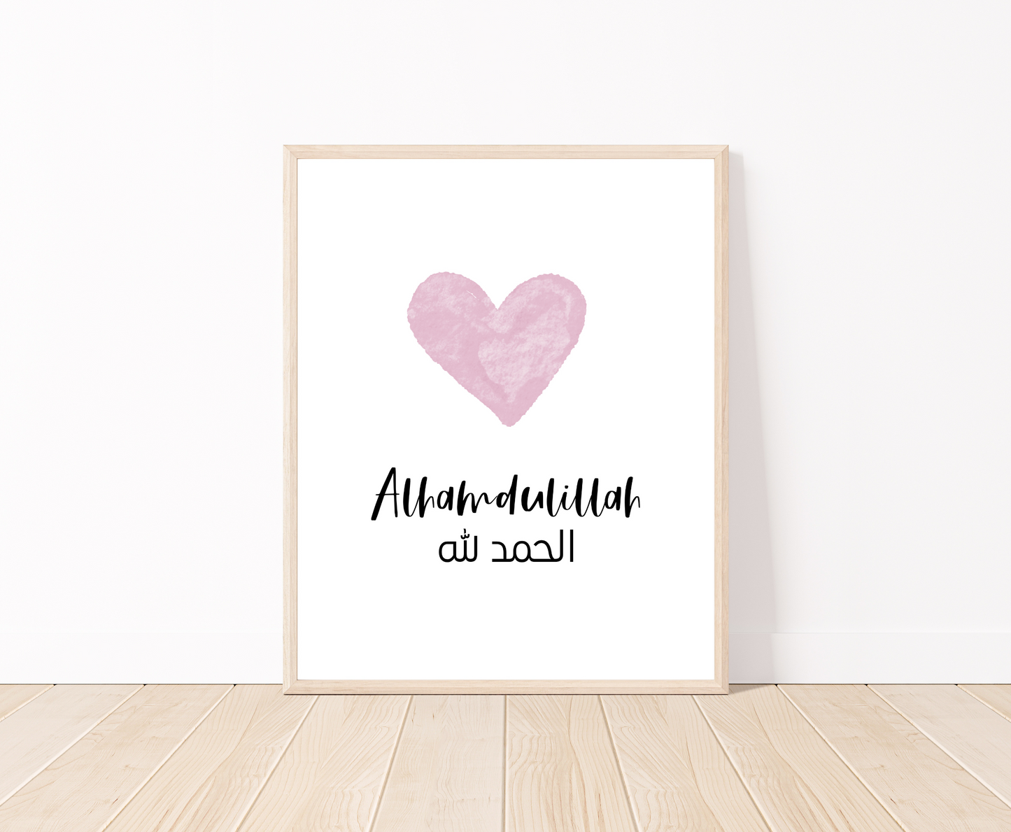 A digital print placed on a white wall and parquet flooring showing a pink heart with a piece of writing below that says: “Alhamdulillah”.