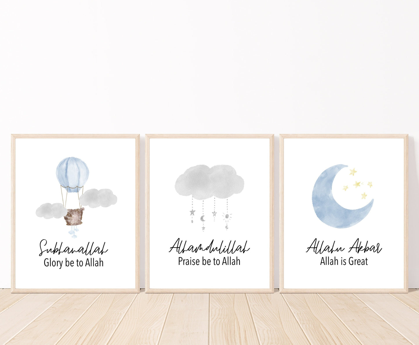 Three frames with three different graphics that are placed on a white wall and parquet flooring. The first one shows an air balloon with the word “Subhanallah”, Glory Be to Allah, written below. The middle one shows a gray cloud design with the word “Alhamdulillah”, Praise Be to Allah below. The last one shows a baby blue crescent and tiny yellow stars with the word “Allahu Akbar”, Allah is great, written below.