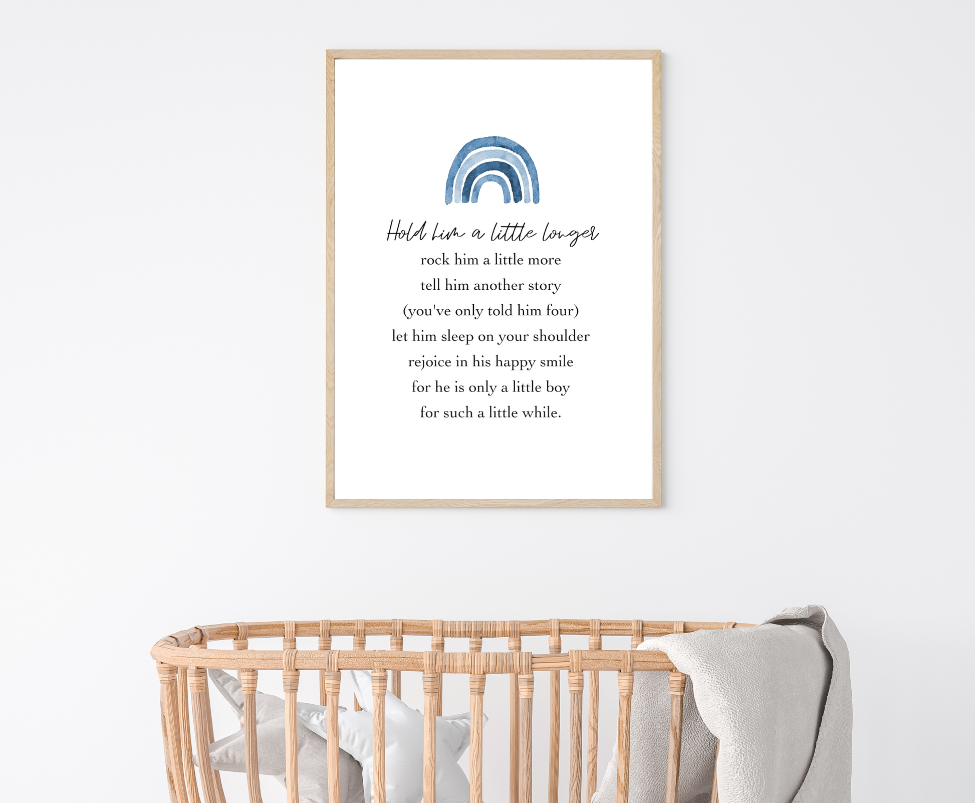 A digital print is hung above a baby’s cradle. The digital print has a blue rainbow at the top and a piece of writing that says: Hold him a little longer, rock him a little more, tell him another story, (you have only told him four), let him sleep on your shoulder, rejoice in his happy smile, for he is only a little boy, for such a little while.