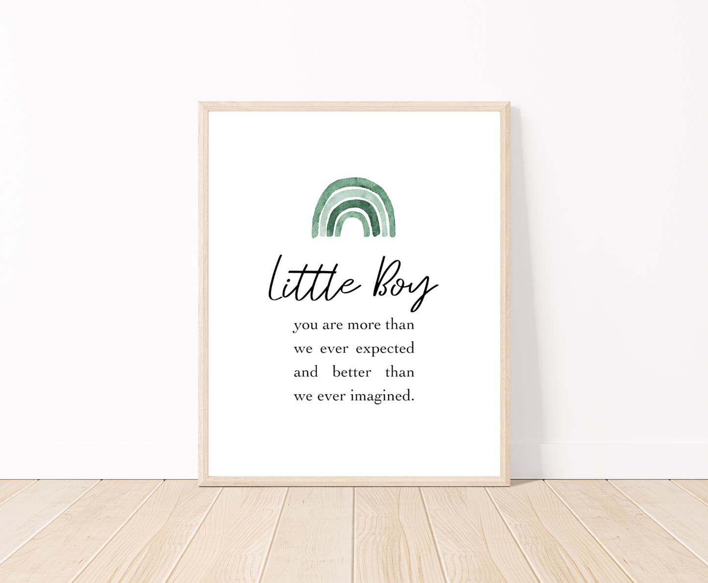 A frame showing a graphic for a little boy’s room displaying a rainbow design in different shades of green  and includes a piece of writing that says: Little boy, you are more than we ever expected and better than we ever imagined. The frame is placed on a parquet floor.
