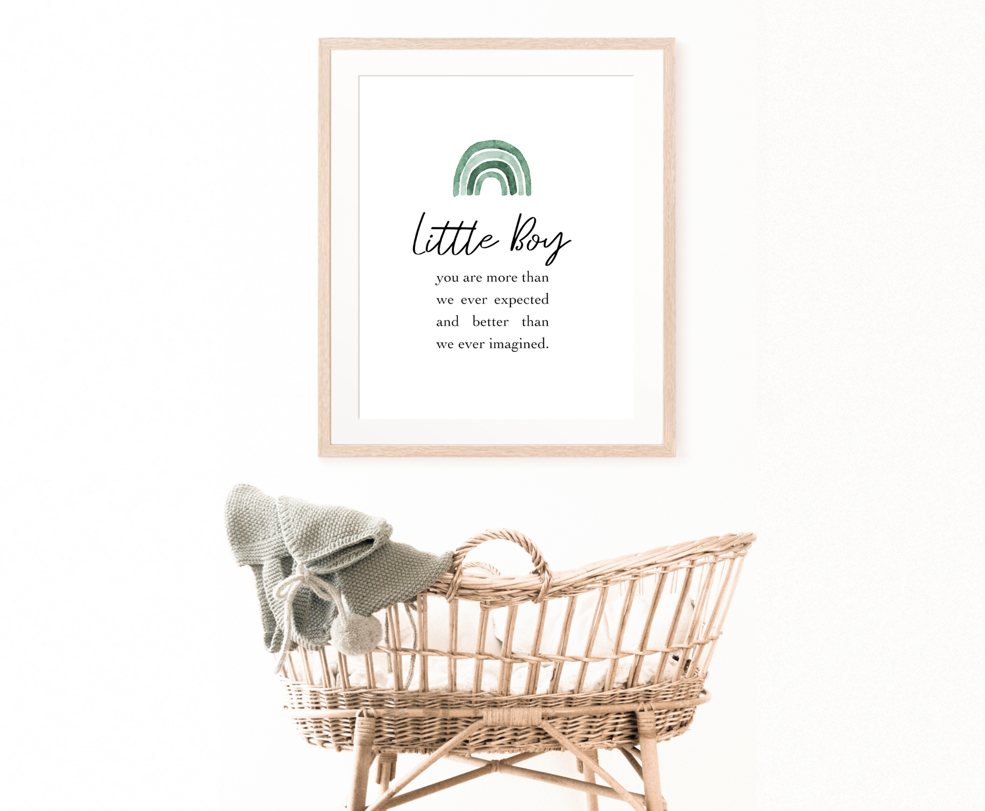 An image of a cradle with a frame hanging on the wall behind it. The frame shows a graphic for a little boy’s room displaying a rainbow design in different shades of green  and includes a piece of writing that says: Little boy, you are more than we ever expected and better than we ever imagined.