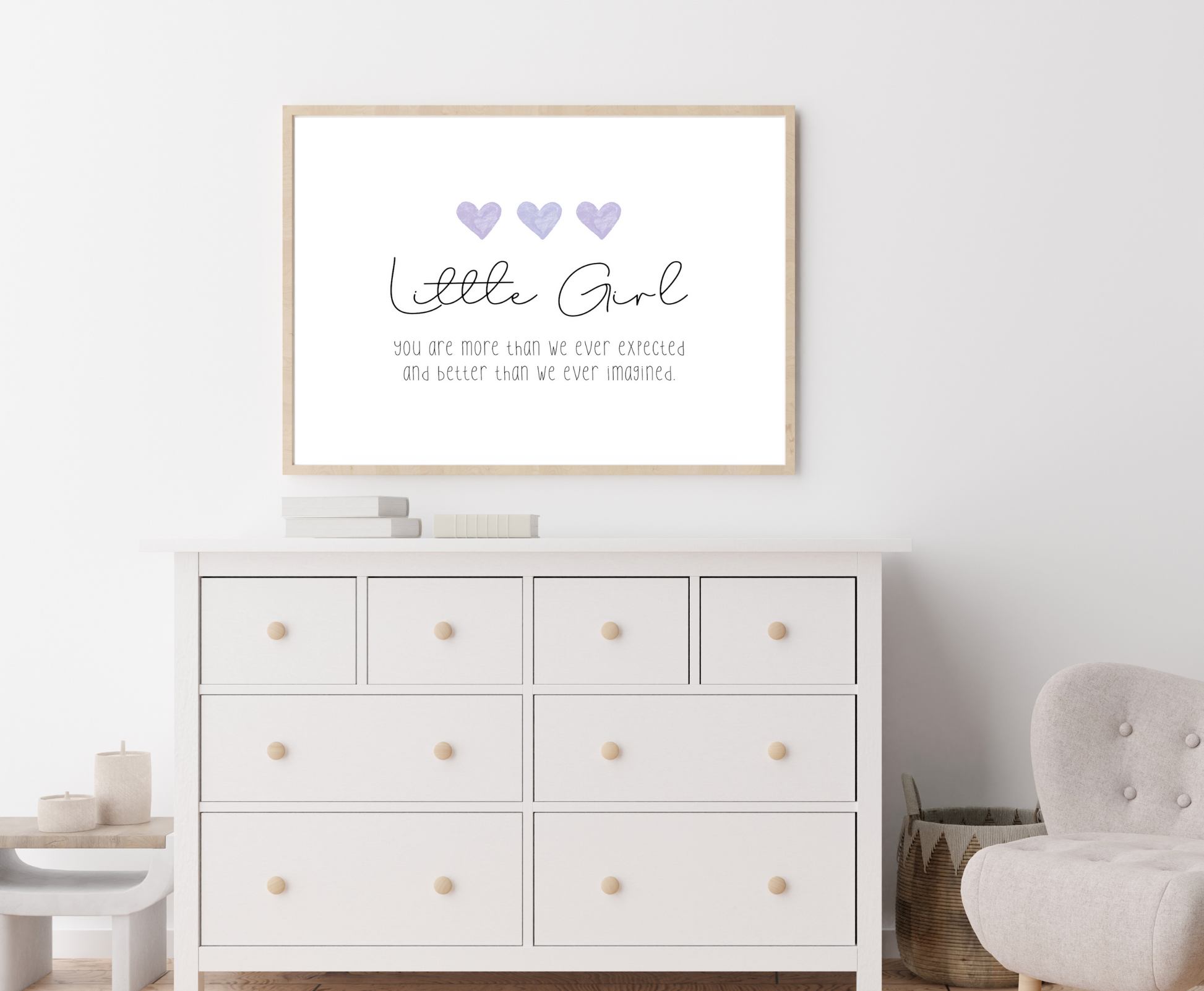 An image of a white dresser with a frame hanging on the wall behind it. The frame displaying a digital graphic that has three purple blue heart and a piece of writing below that says: little girl you are more than we ever expected and better than we ever imagined. 