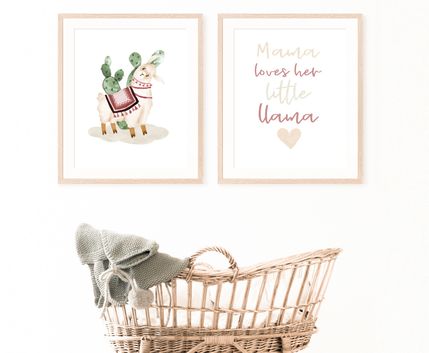 A cradle with two digital frames hanging on the wall behind it. The first one displays an illustration of a cute lama wearing a red tapestry with a green cactus right behind it, while the other one includes a piece of writing in bold baby pink, grey, and red that says “Mama loves her little llama”.