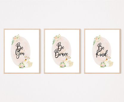 Three identical digital graphics but have different writings showing a baby pink oval shape decorated with flowers on the top and the bottom of the shape and beside the flowers at the bottom there is a cute goose illustration. The first graphic says” Be Brave”, the second “Be Kind”, and the third “Be You”.