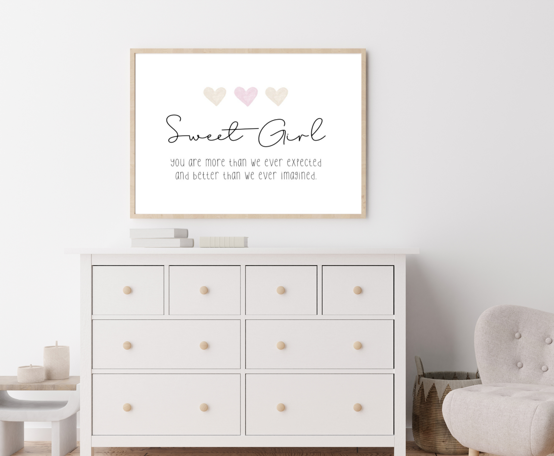 A picture showing a white dresser with a little girl’s graphic hanging on the wall right above the latter. The graphic is showing three pink and beige hearts with a piece of writing below that says: Sweet girl you are more than we ever expected, and better than we ever imagined.
