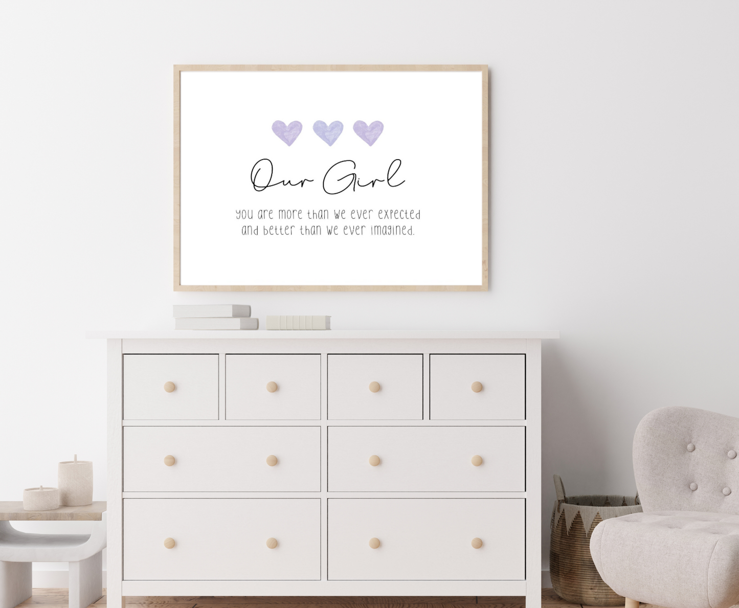 A picture showing a white dresser with a little girl’s graphic hanging on the wall right above the latter. The graphic is showing three purple blue hearts with a piece of writing below that says: Our girl, you are more than we ever expected, and better than we ever imagined.