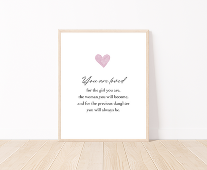 A digital poster is placed on a white wall and parquet flooring and has a pink heart at the top with a piece of writing that says: “You are loved for the girl you are, the woman you will become, and for the precious daughter you will always be.”