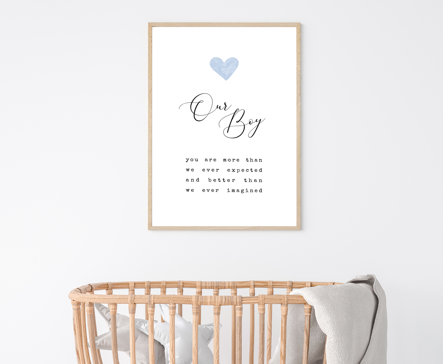 A little boy’s room digital print that is hung above a baby’s cradle and has a baby blue heart at the top, and a piece of writing that says: “Our boy, you are more than we ever expected and better than we ever imagined.”