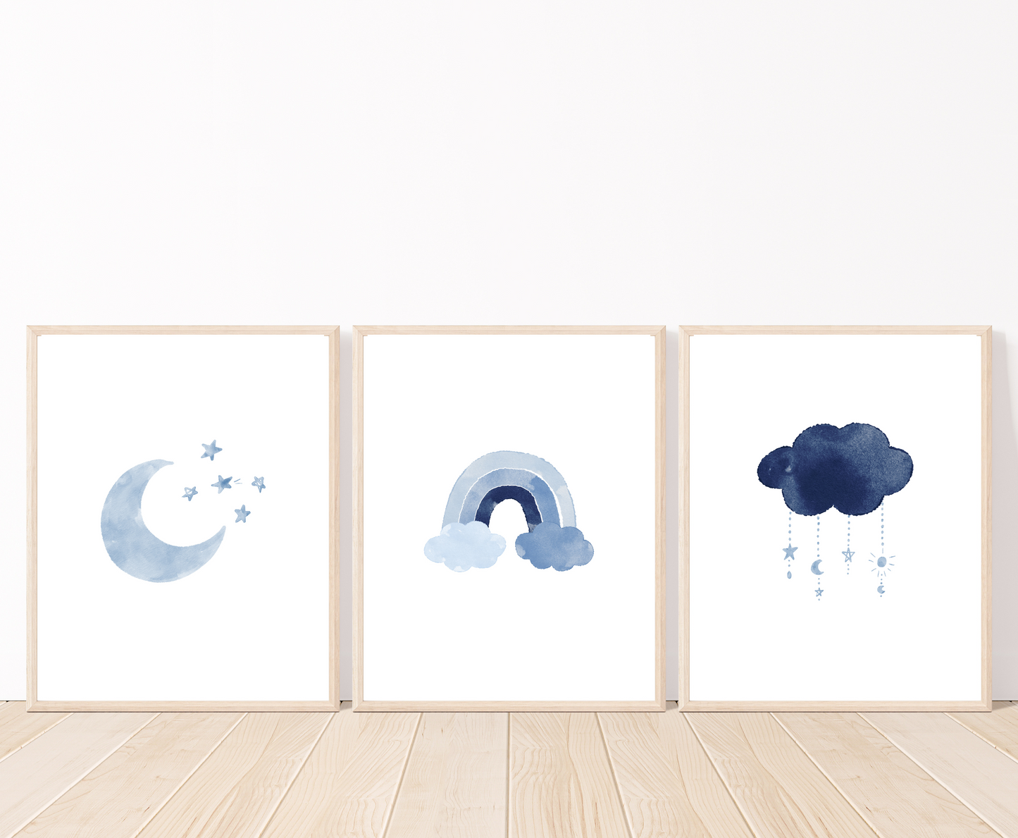 Three frames showing blue graphics that are placed on a white wall and parquet flooring. The first one shows a blue crescent moon with tiny blue stars right beside it. The second one shows a rainbow in different shades of blue. The third frame shows a dark blue cloud with tiny blue crescent moons and stars dangling from it.