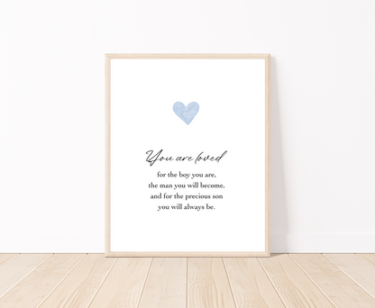 A digital poster is placed on a white wall and parquet flooring and has a blue heart at the top with a piece of writing that says: “You are loved for the boy you are, the man you will become, and for the precious son you will always be.”