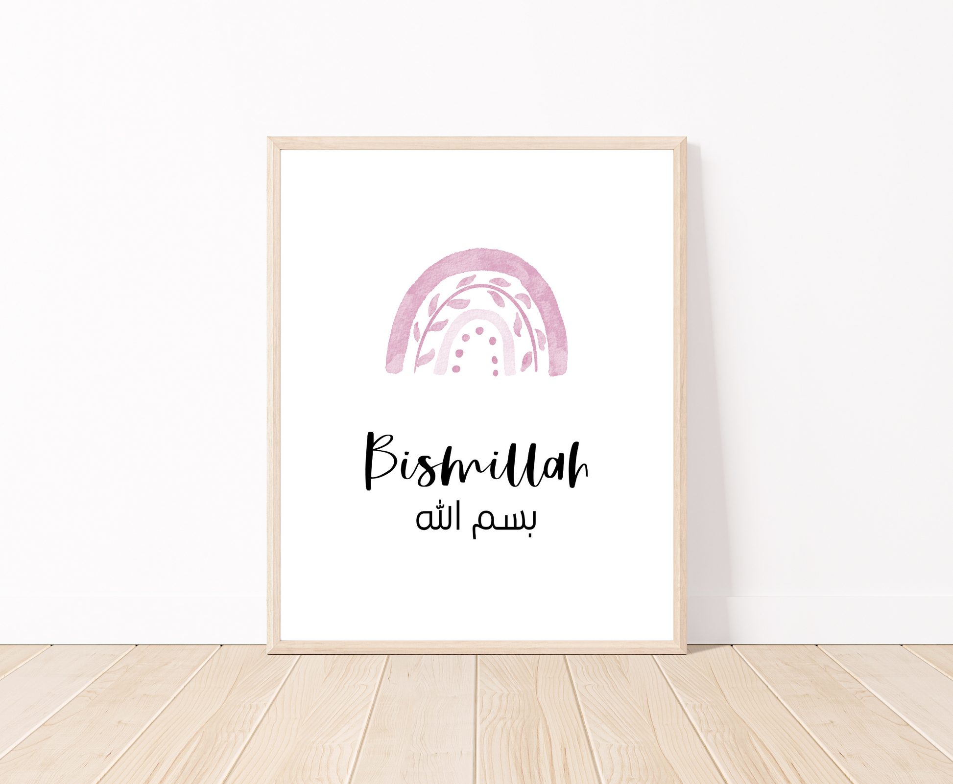 A digital print placed on a white wall and parquet flooring showing a pink rainbow with a piece of writing below that says: “Bismillah”.