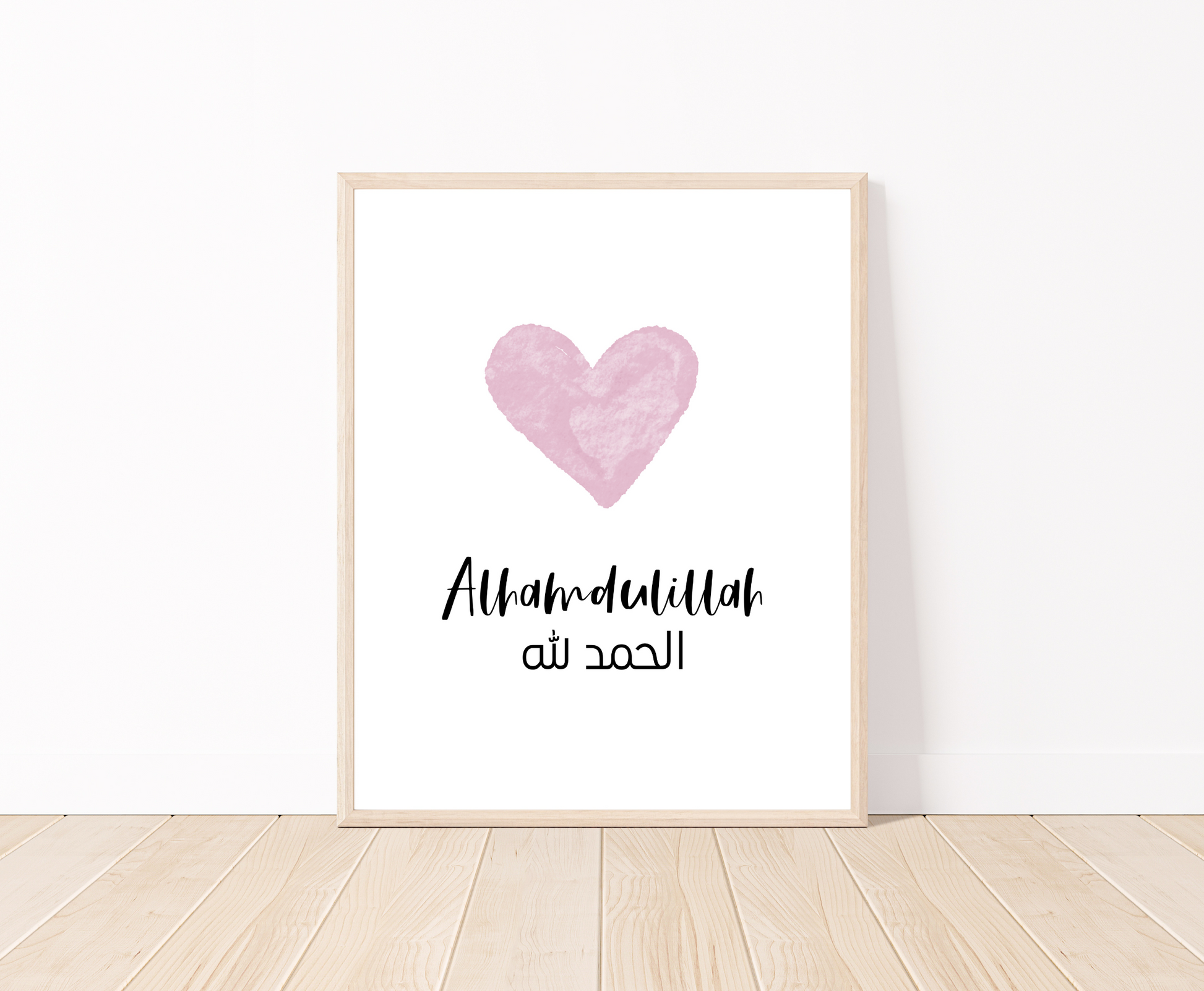 A digital print placed on a white wall and parquet flooring showing a pink heart with a piece of writing below that says: “Alhamdulillah”.