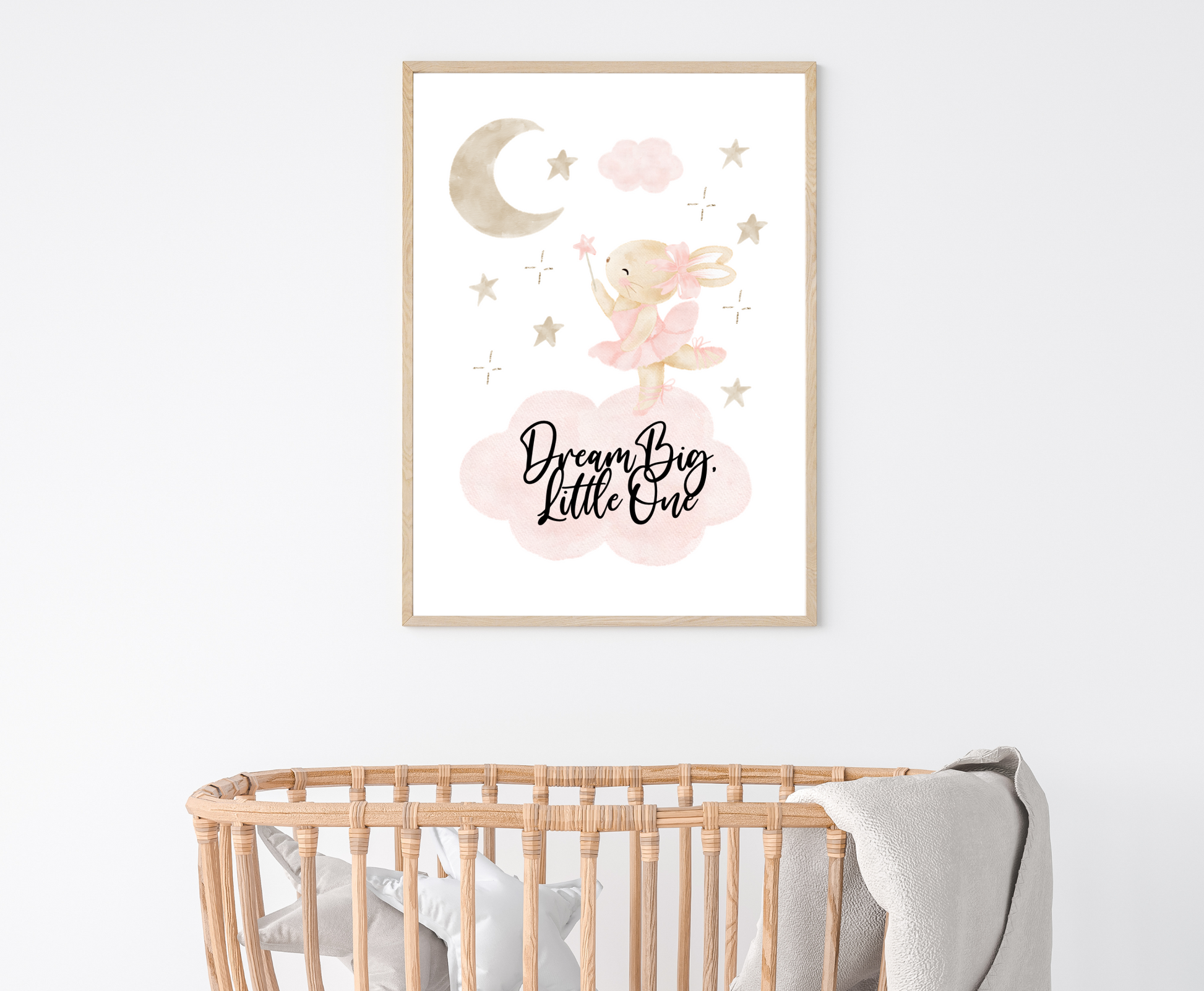 A little girl’s room graphic hanging above a baby’s cradle and showing a grey-pinkish crescent with a brown teddy rabbit wearing a pink bow, with a few tiny grey-pinkish stars beside it and two pinkish clouds. It also includes a piece of writing that says “Dream Big Little One”.