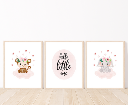 A picture of three digital printable graphics placed on a white wall and parquet flooring. The first one shows a graphic of a cute baby monkey with a flower crown on its head and sitting on a pink cloud with mini stars surrounding it. The middle one has a piece of writing inside a pink oval shape that says “Hello little one”. The last one shows a cute baby elephant printing with a flower crown on its head and sitting on a pink cloud with mini stars surrounding it.