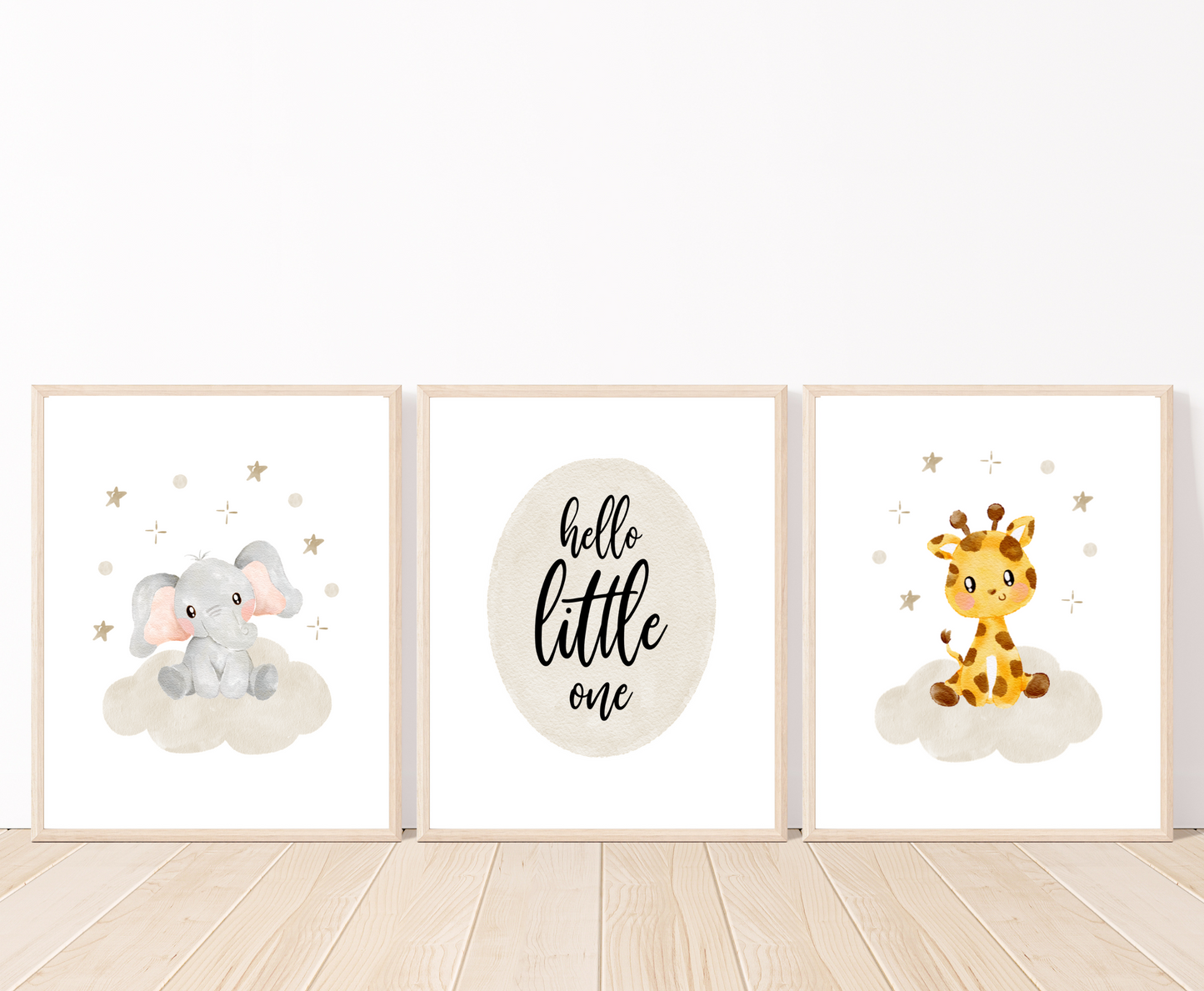 A picture of three digital printable graphics placed on a white wall and parquet flooring. The first one shows a graphic of a grey baby elephant sitting on a grey cloud with mini stars surrounding its head. The middle one has a piece of writing inside a grey oval shape that says “Hello little one”. The last one shows a cute baby giraffe sitting on a grey cloud with mini stars surrounding its head.