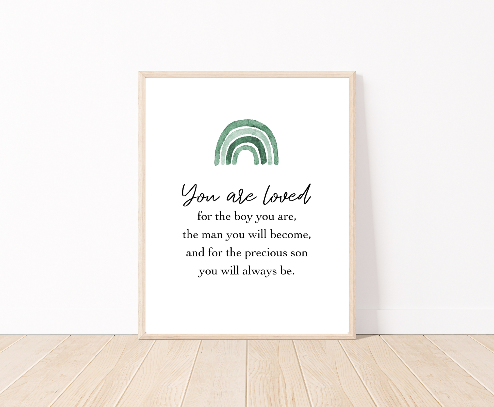 A frame placed on the floor showing a graphic for a little boy’s room that has an ombre green rainbow design and includes the following “You are loved, for the boy you are, the man you will become, and for the precious son you will always be”.