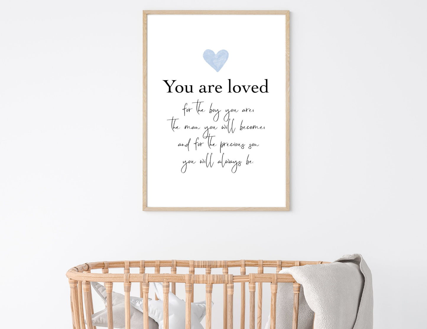 A digital print is hung above a baby’s cradle. The digital print has a baby blue heart at the top and a piece of writing that says: “You are loved for the boy you are, the man you will become, and for the precious son you will always be.”