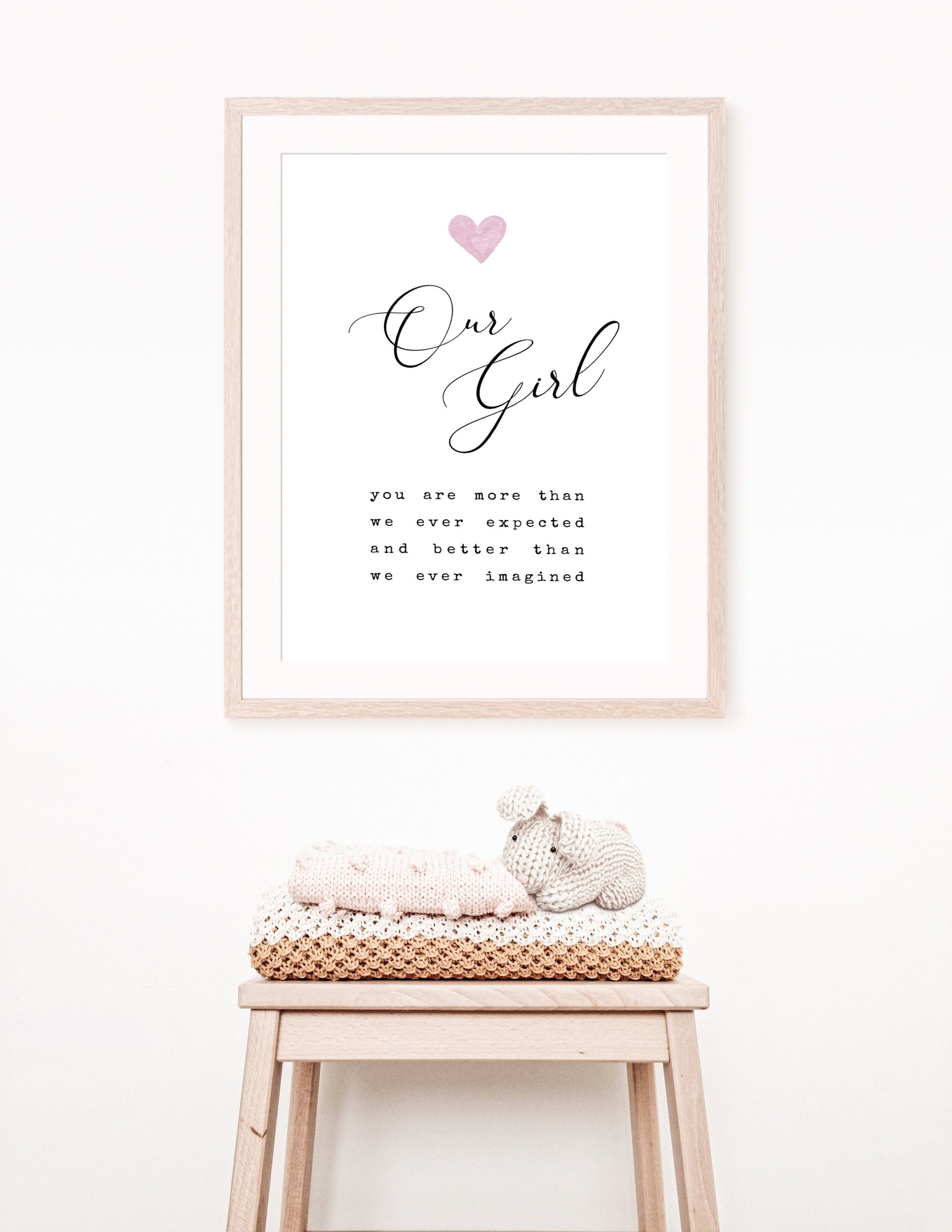 A digital print is hung above a baby’s desk. The digital print has a pink heart at the top, and a piece of writing that says: “Our girl, you are more than we ever expected and better than we ever imagined.”