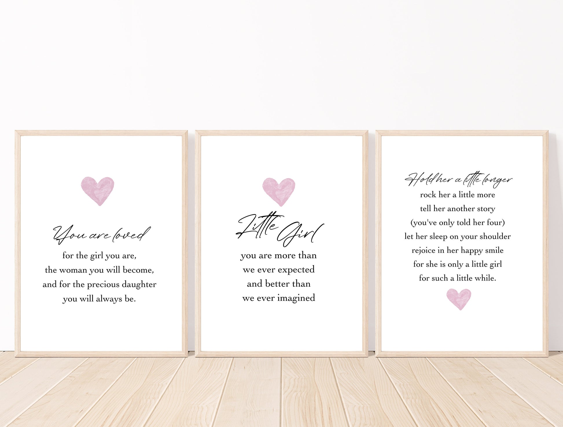 Three frames for a baby girl’s room graphics that are placed on a white wall and parquet flooring. The first one shows a pink heart with a piece of writing below that says: You are loved for the girl you are, the woman you will become, and for the precious daughter you will always be. The middle graphic shows a pink heart with a piece of writing below that says: little girl you are more than we ever expected and better than we ever imagined. The last one has the heart below the piece of writing.