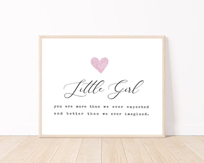 A little girl’s room horizontal digital print placed on a white wall and parquet flooring that has a pink heart at the top, and a piece of writing that says: “Little girl, you are more than we ever expected and better than we ever imagined.”