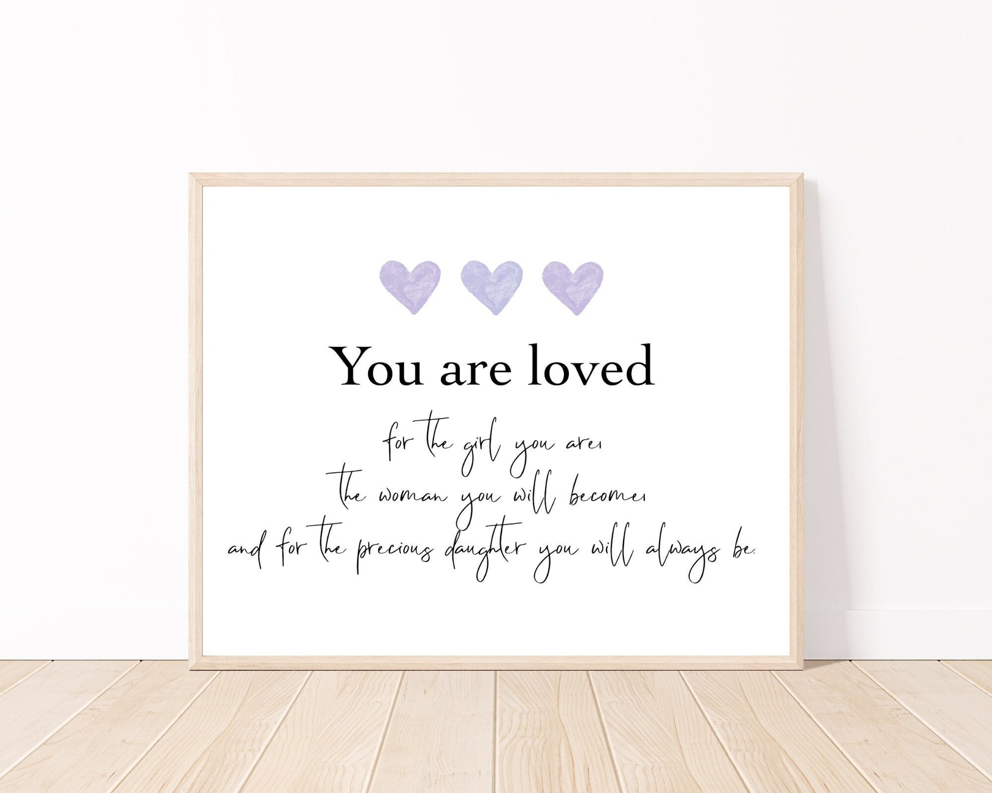 A little girl’s room digital poster that is placed on a white wall and parquet flooring and has three purple hearts at the top with a piece of writing that says: “You are loved for the girl you are, the woman you will become, and for the precious daughter you will always be.”