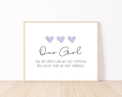 A little girl’s room digital print placed on a white wall and parquet flooring that has three purple hearts at the top, and a piece of writing that says: “Our girl, you are more than we ever expected and better than we ever imagined.”