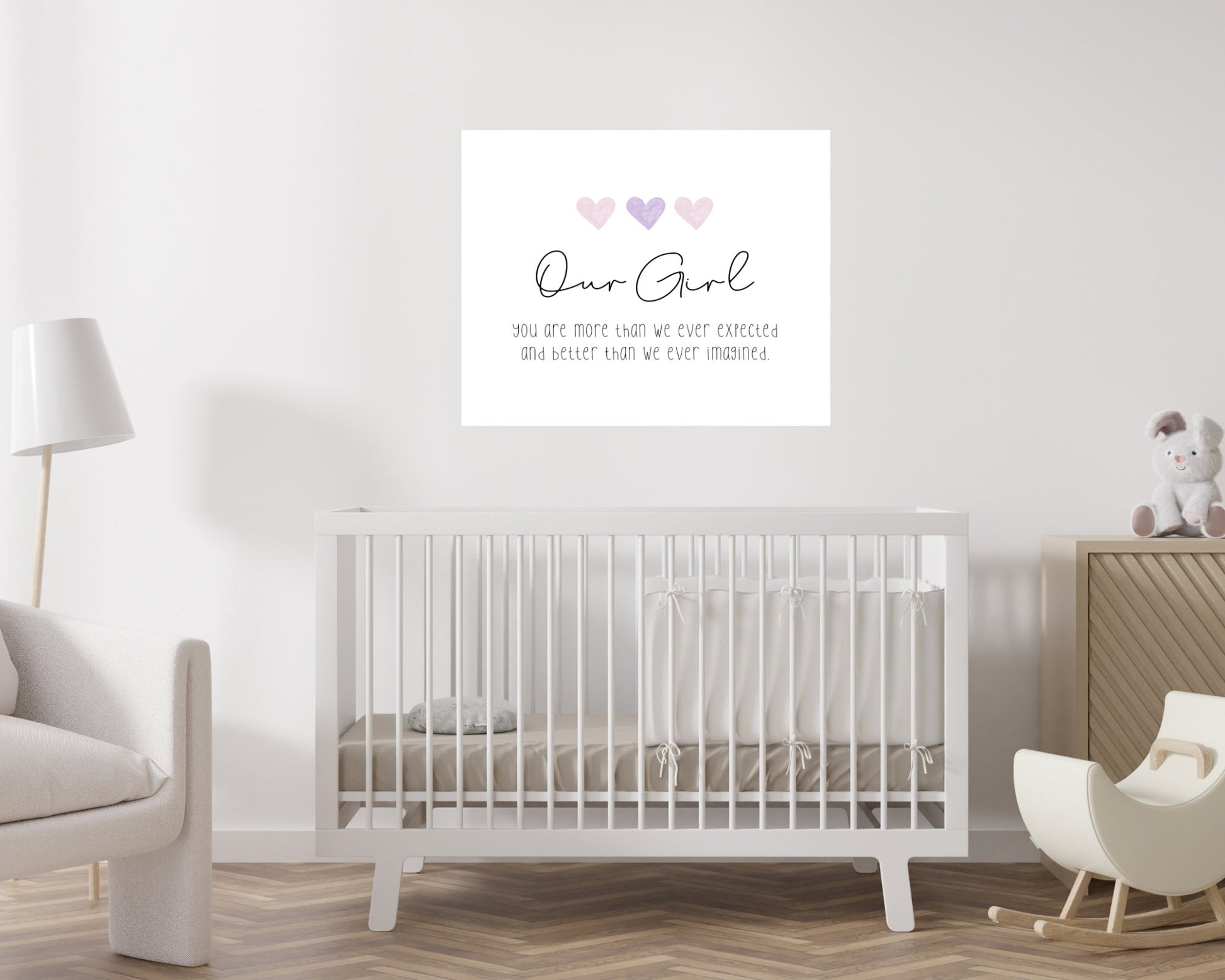 A digital print is hung above a baby’s cradle. The digital print has three hearts at the top, and a piece of writing that says: “Our girl, you are more than we ever expected and better than we ever imagined.”